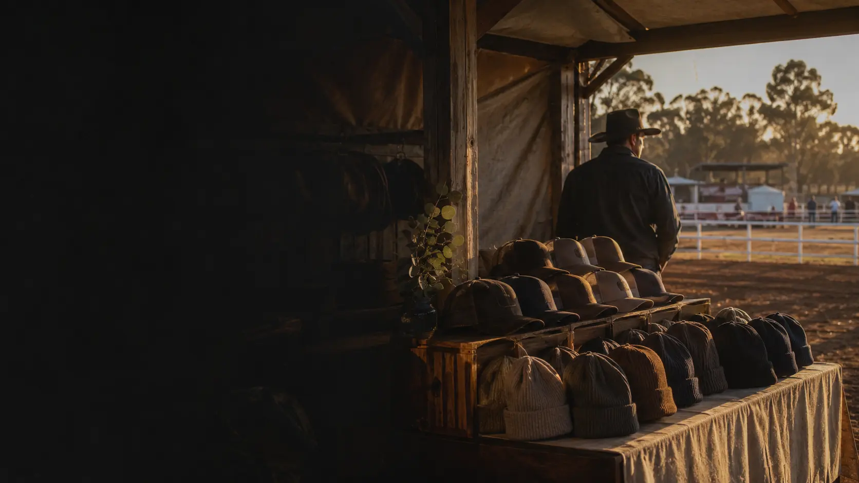 A country clothing pop up shop at a showground at sunrise, caps and beanies laid out along a timber trestle